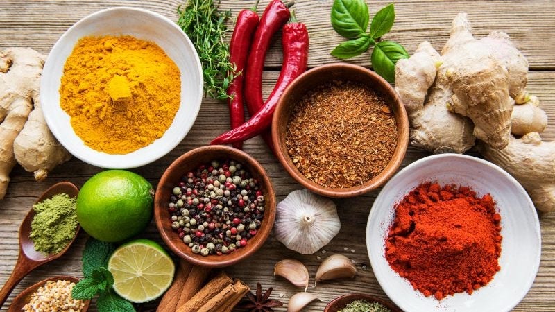 A selection of various colorful spices on a wooden table in bowls and spoons.