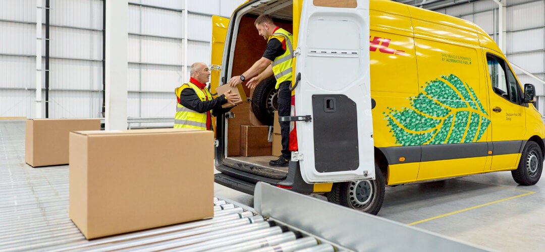 Two DHL employees load shipping boxes into a DHL yellow van