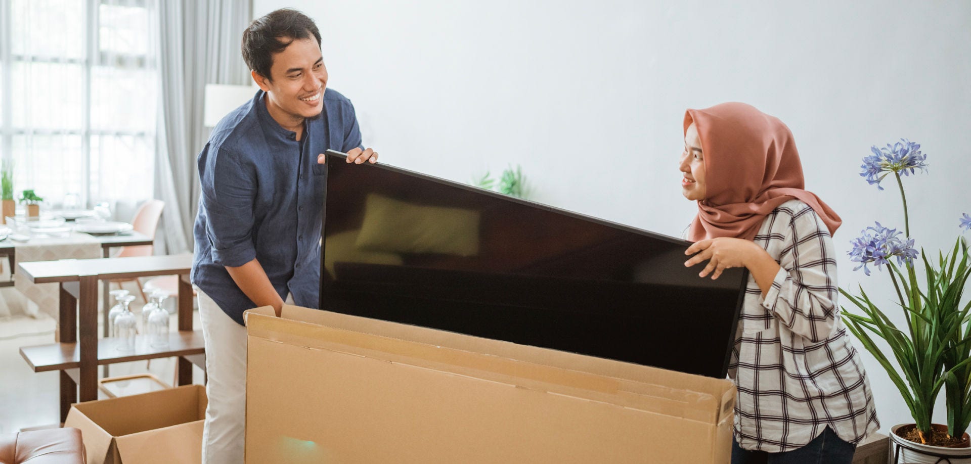 couple working together to load a large television into a shipping box
