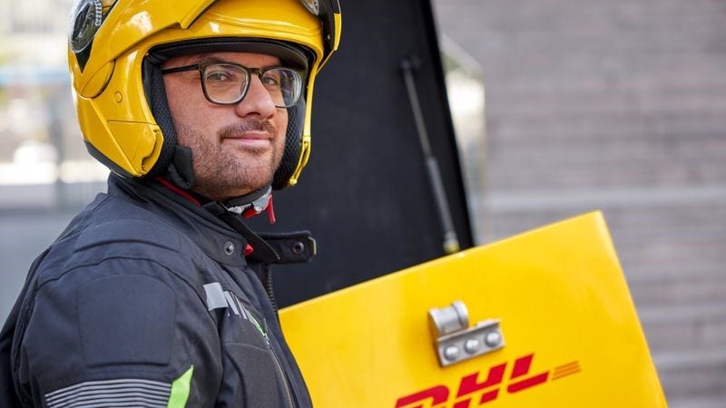 A male DHL employee is standing next to his motorbike.