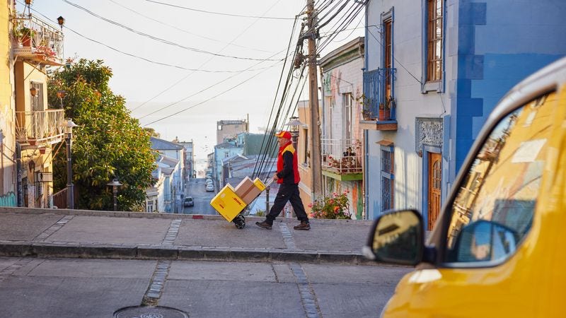 Male DHL employee pushing trolley of goods and packages through colourful streets of Saudi Arabia