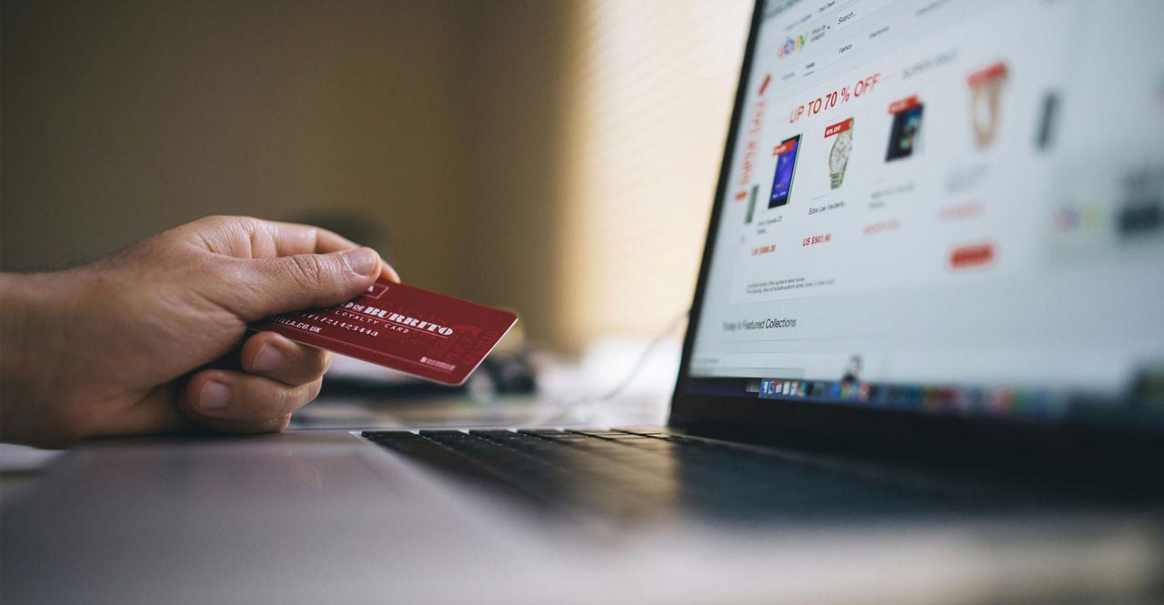 A consumer holds a credit card in front of a laptop while going through the e-commerce checkout process