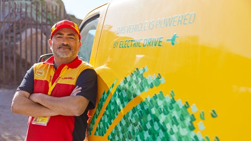 a male dhl employee leaning on an electric van that promotes sustainable logistics