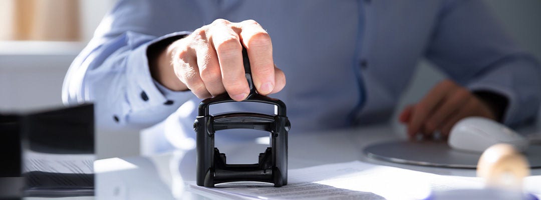 Nærbillede af en persons håndstempling med godkendt stempel på dokument ved skrivebordet