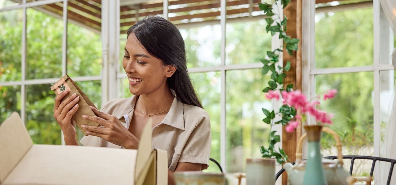 A female customer is sitting at a table nearby, smiling as she looks at the inside of her parcel.