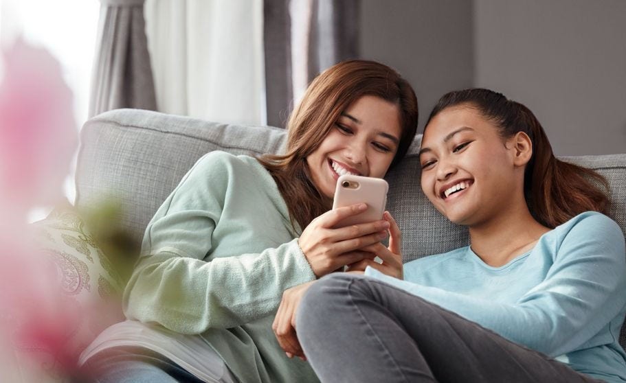 Two women smiling while shopping online together on a smartphone