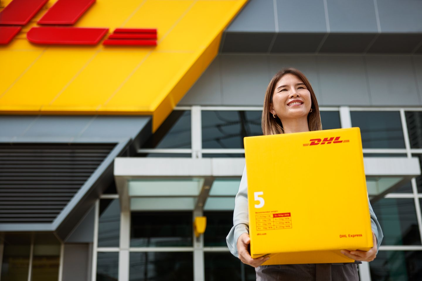 female customer stands in front of the DHL ServicePoint after picking up her parcel