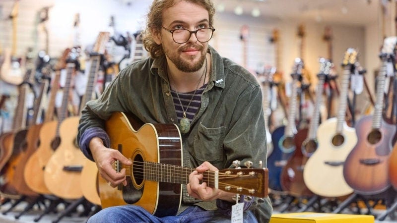 Inline Static ( 800x450)  - A male music store owner plays the guitar, sitting next to a DHL parcel inside a music store.