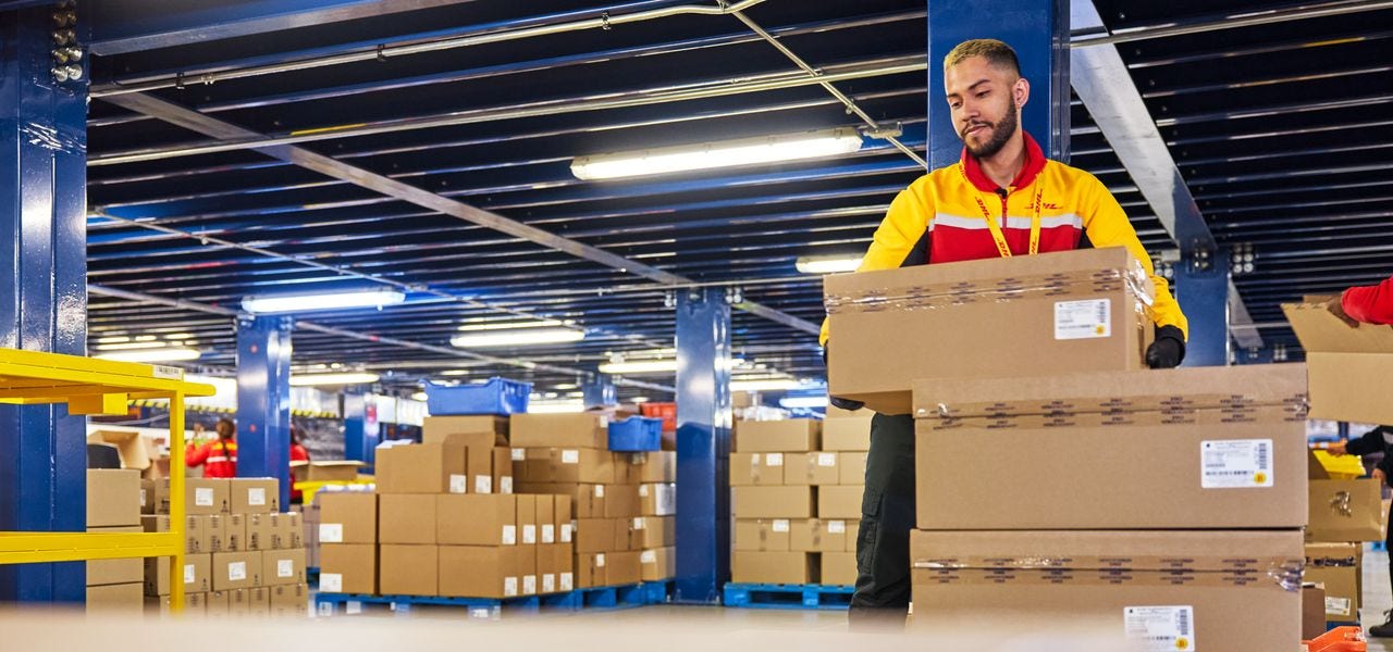 Male DHL employees carrying packed parcel onto pallets at Teva Warehouse.