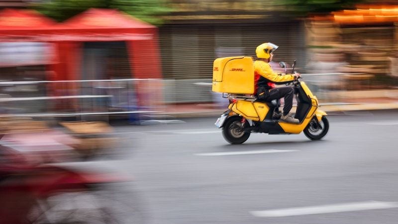 a DHL Express deliveryman zooming by the street on his motorbike