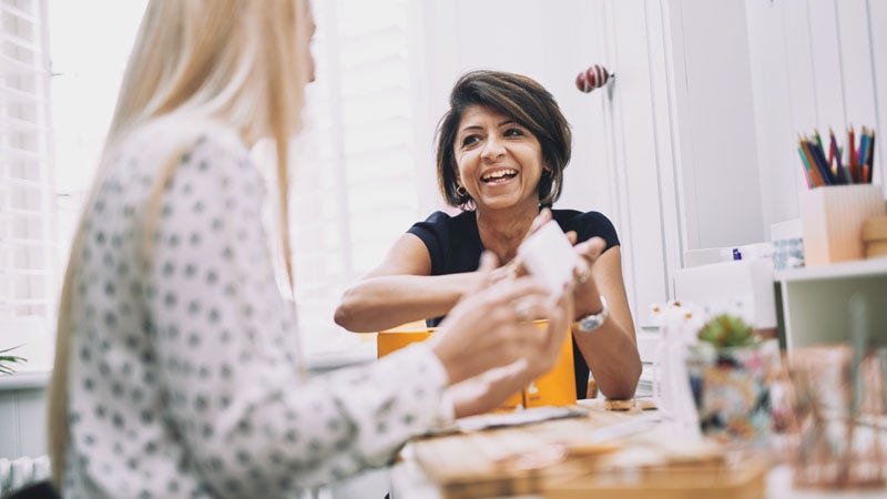 woman smiling at another woman whilst holding a white box.