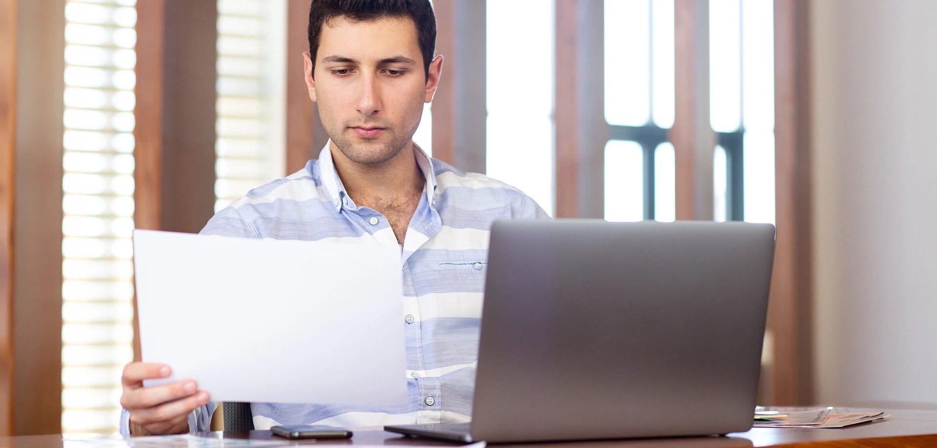 Hombre trabajando con su laptop y una hoja de papel en un escritorio