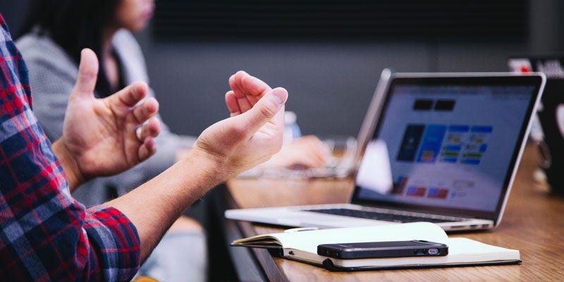 Man gesturing in front of a macbook and a notepad and iphone on the desk