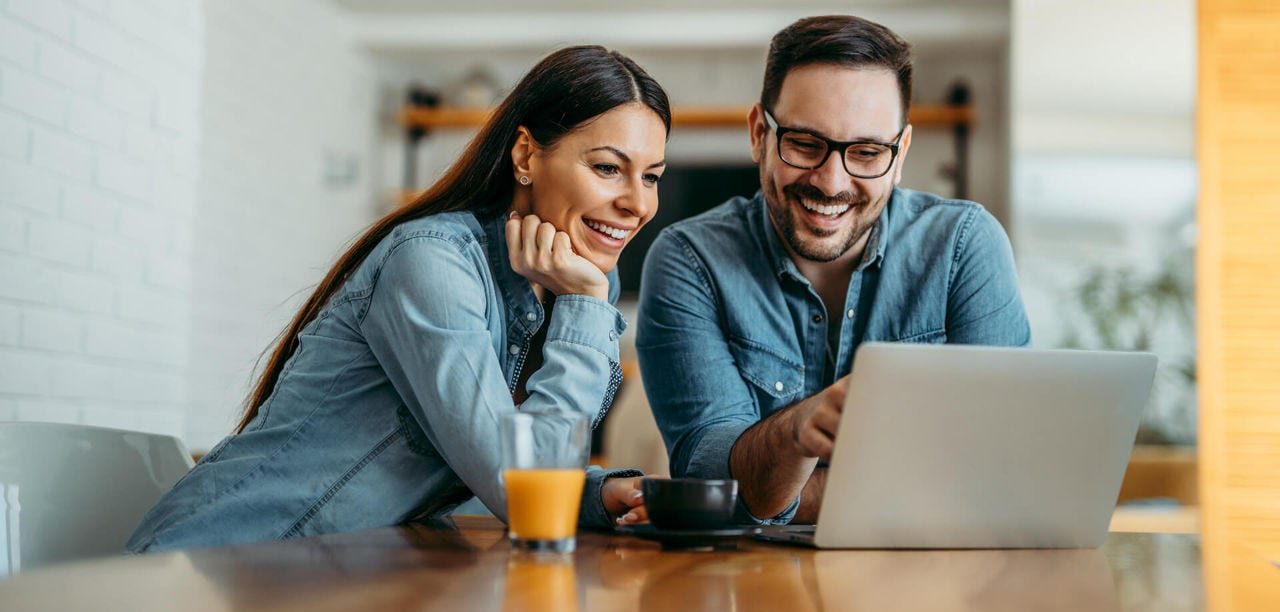 young couple sitting together looking at their laptop screen, smiling