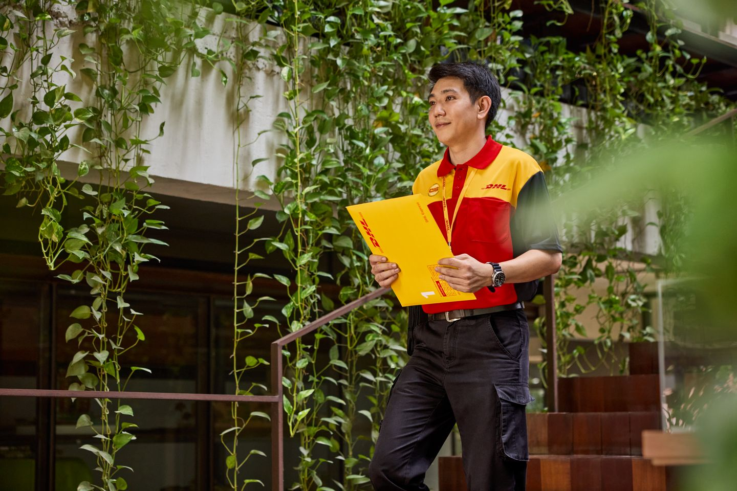 male DHL employee walking down the stairs in an office while carrying an express envelope