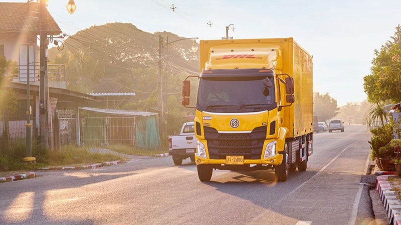 DHL electric truck driving on a street at sunrise for delivery