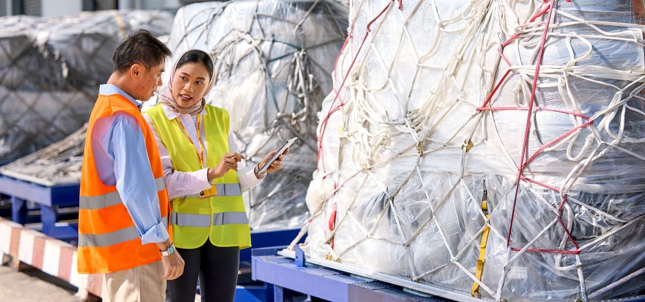 A female DHL expert with tablet in her hand and a male DHL business customer having a conversation about freigh options at an airfield.
