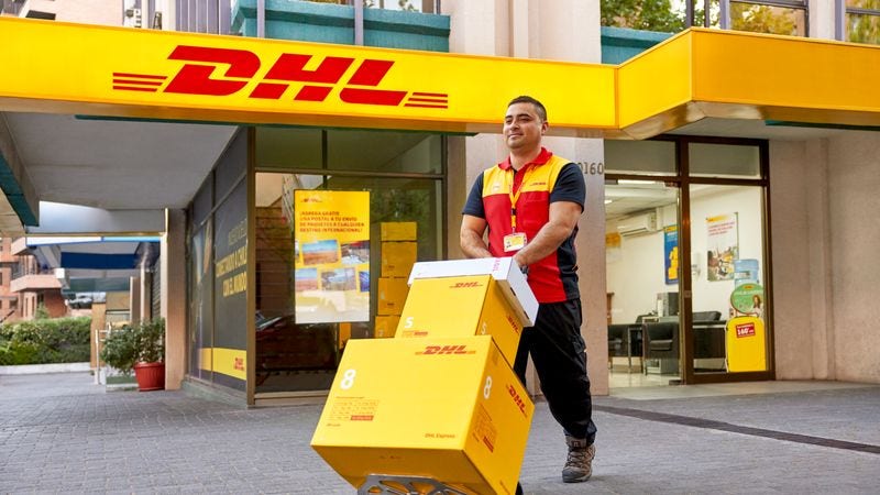 A male DHL employee walking with several food parcels from Thailand on a hand truck.