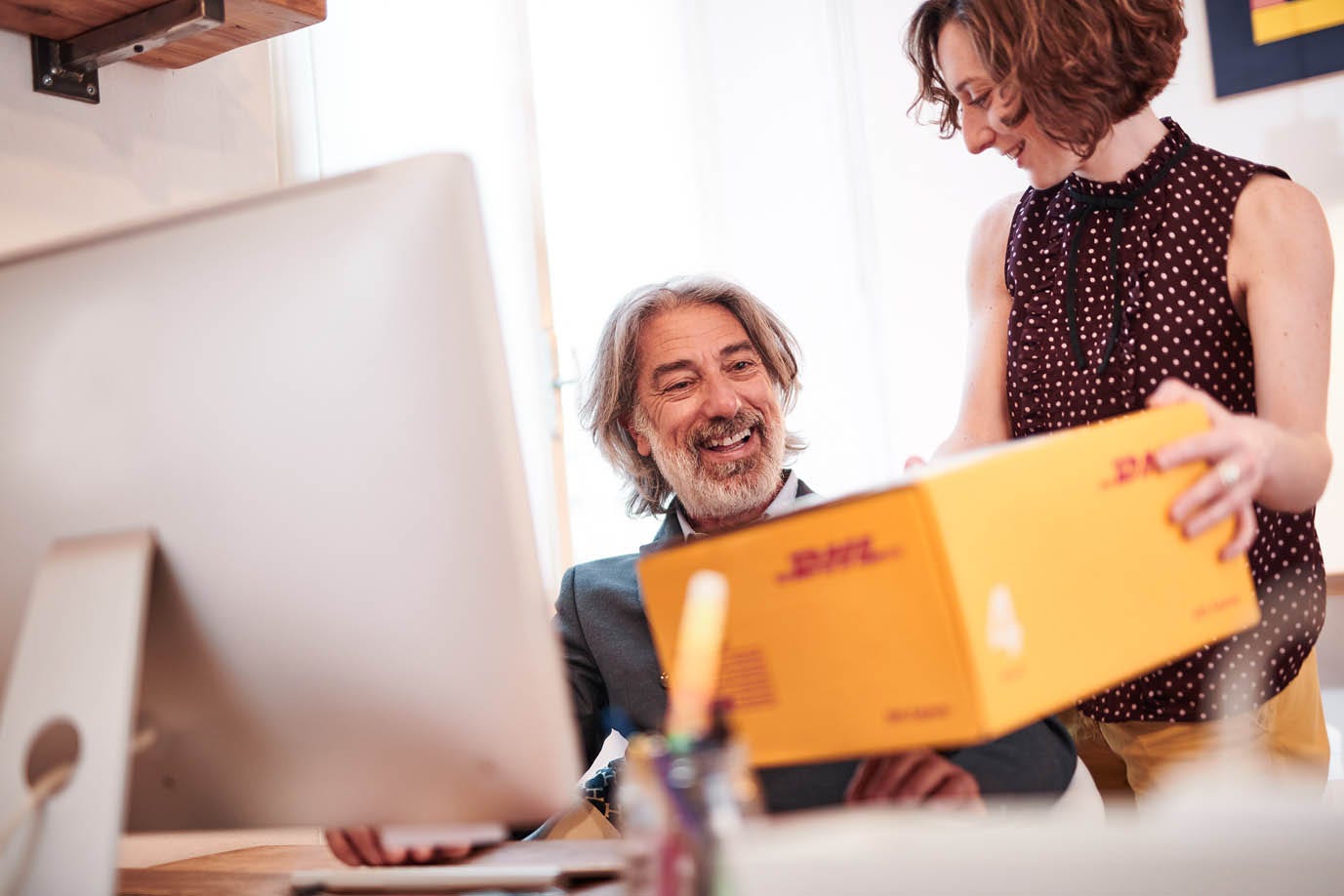 Femme remet à un homme un colis jaune DHL