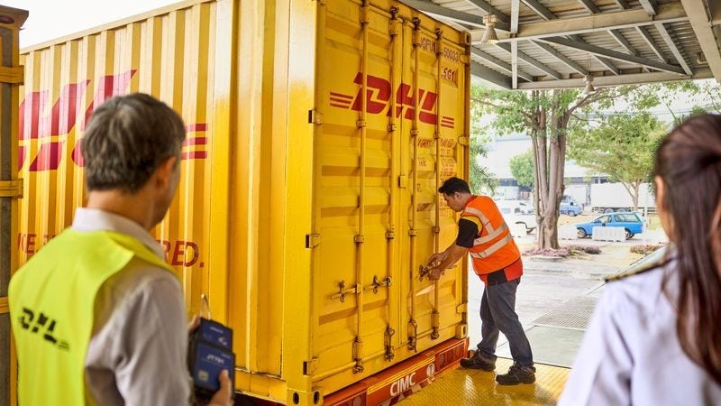 a dhl employee seals a container while being observed by another colleague and a female customs officer.