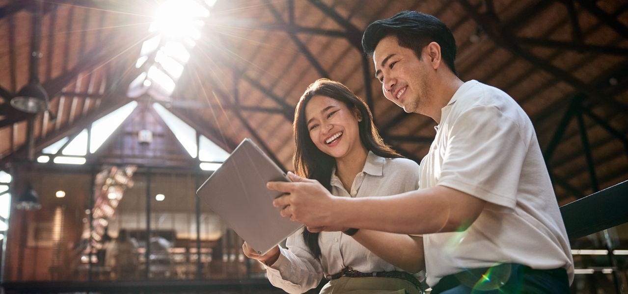 Two DHL employees sit in a sunny area of ​​a sustainable office building and look at a tablet together.