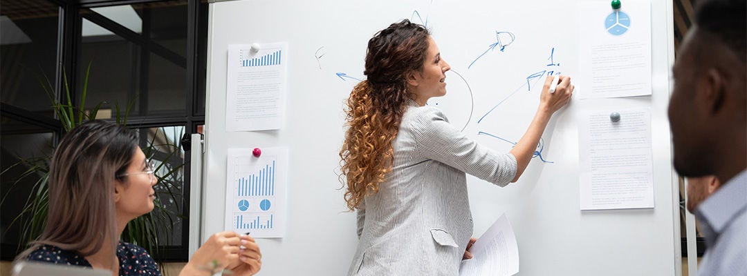 امرأة تكتب على السبورة البيضاء بينما تنظر إليها امرأة أخرى