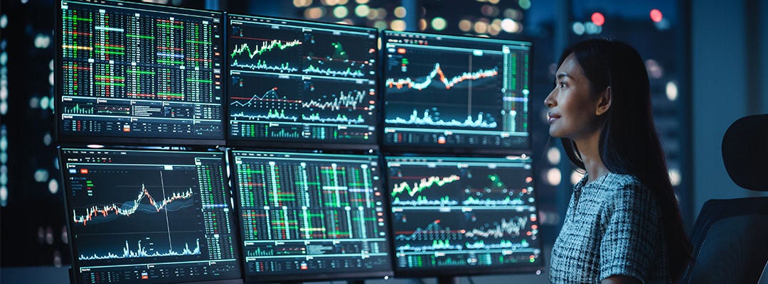 Analyste financier travaillant sur un ordinateur avec une station de travail multi-moniteurs avec des graphiques en temps réel des actions, matières premières et bourses. 