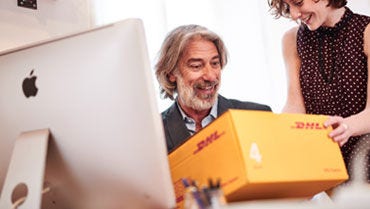 Kobieta wręcza mężczyźnie żółtą paczkę DHL