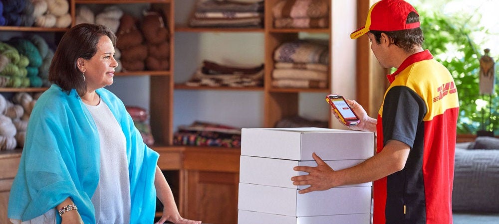 A male DHL employee is scanning parcels for pickup in a wool shop.