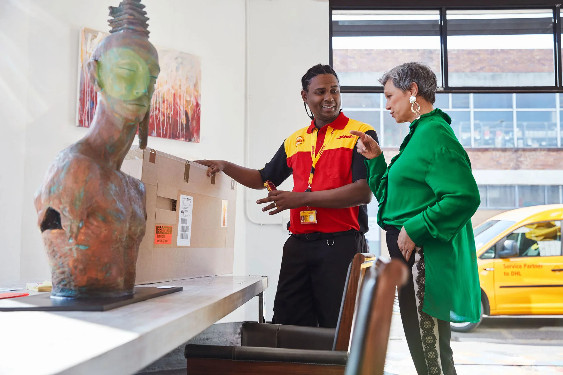 Postman about to pick up package in art gallery, woman points at package
