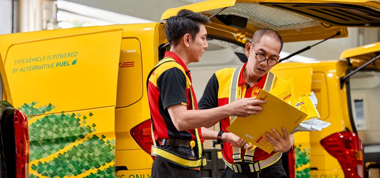 Two male DHL employees are checking the labels of several express envelopes.