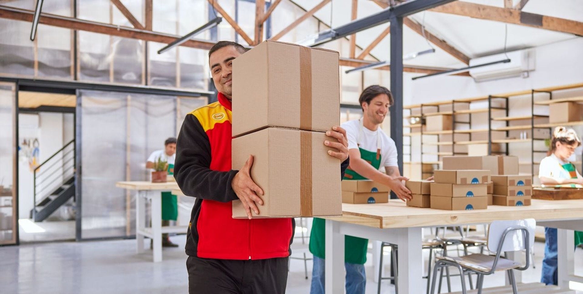 A DHL employee leaves an international business with two parcels for export, while several workers work in the background.