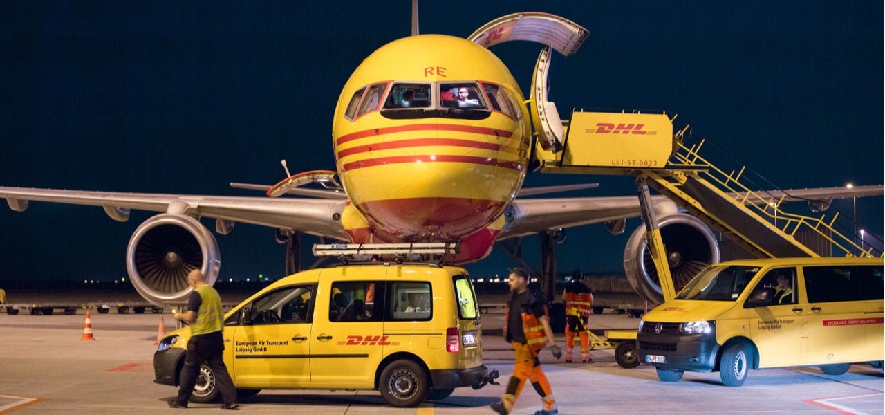 DHL 全货机开启机头货舱，配套品牌工程车与地勤人员开展航空快件装卸作业。