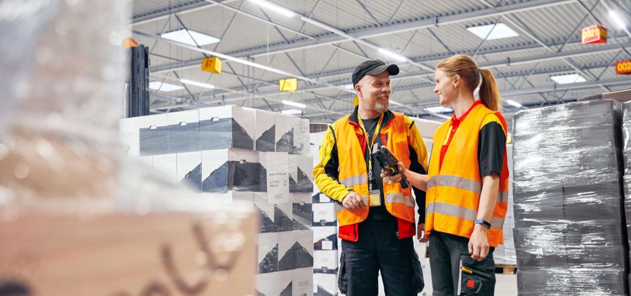 仓库内两名 DHL 一线员工手持扫码设备沟通工作