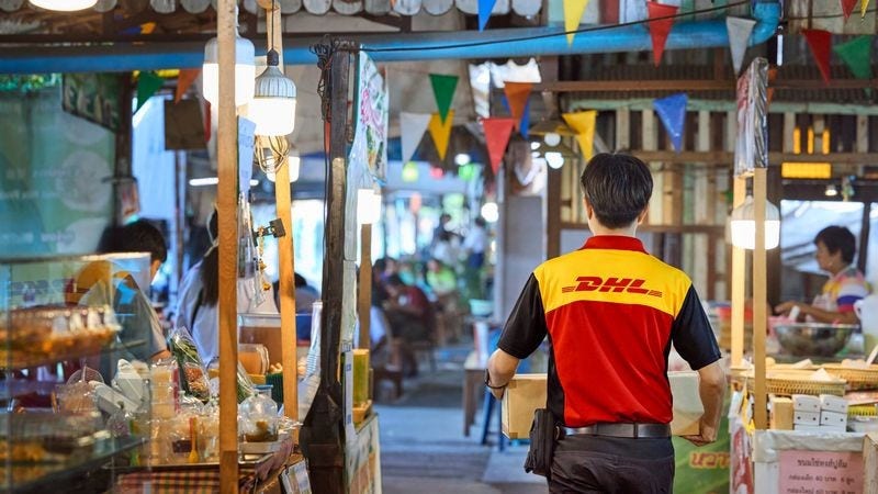 A DHL Express deliveryman walks through a marketplace carrying a parcel.