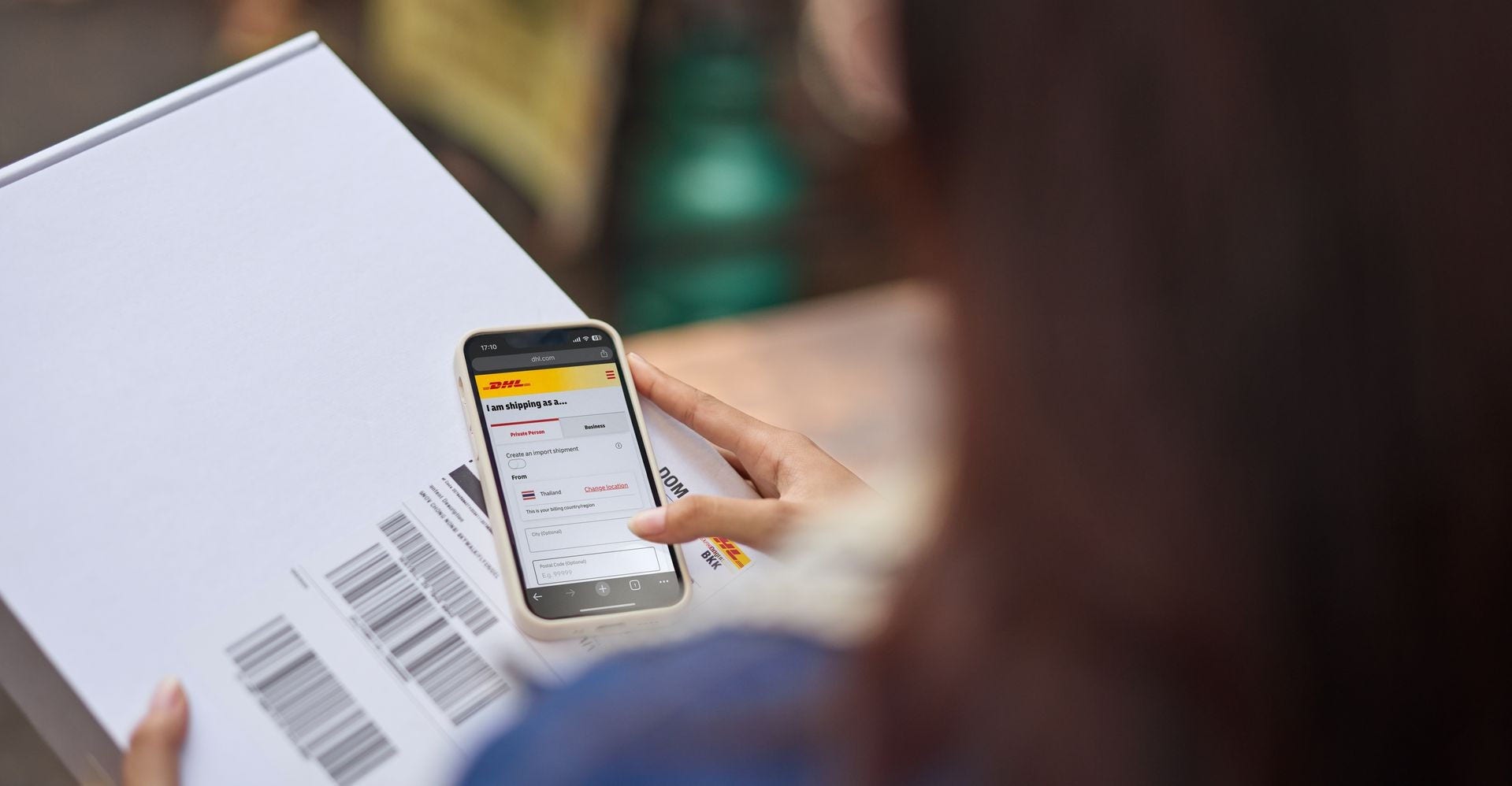 DHL customer using MyDHL+ mobile app while holding a parcel for international shipping