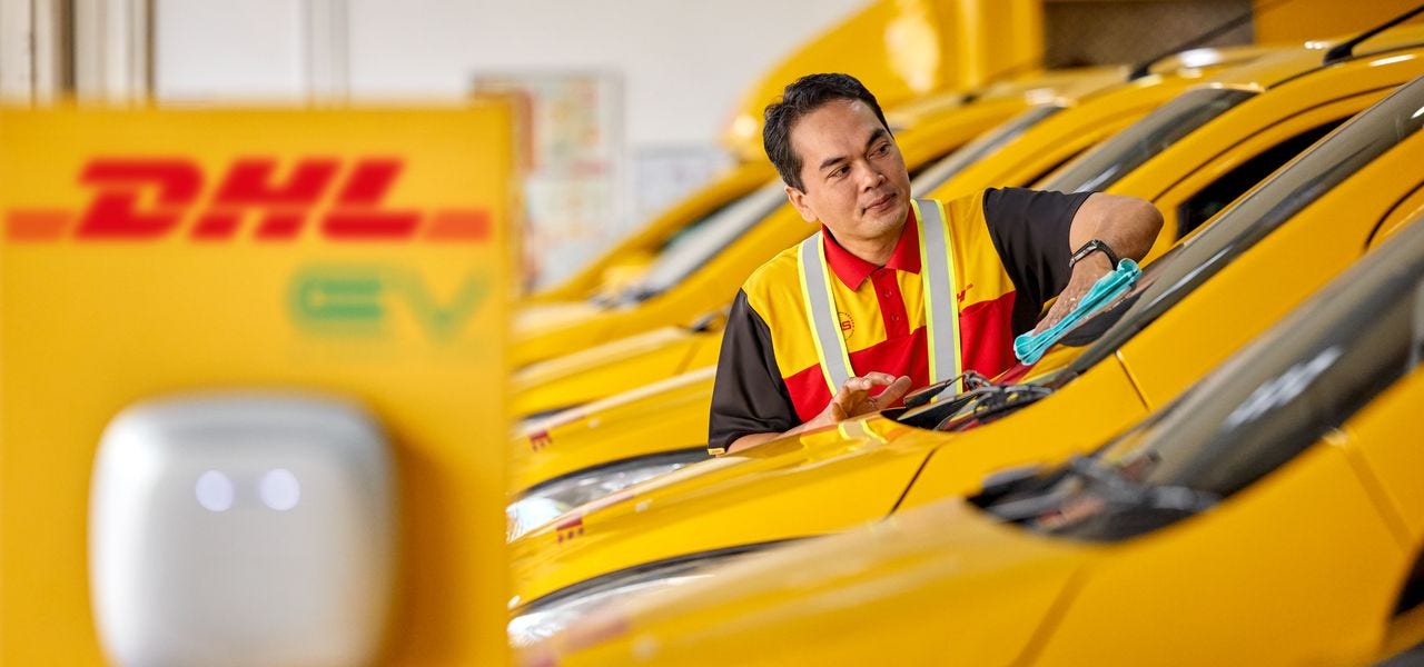 A male DHL employee is cleaning the windshield of an electrical DHL van.