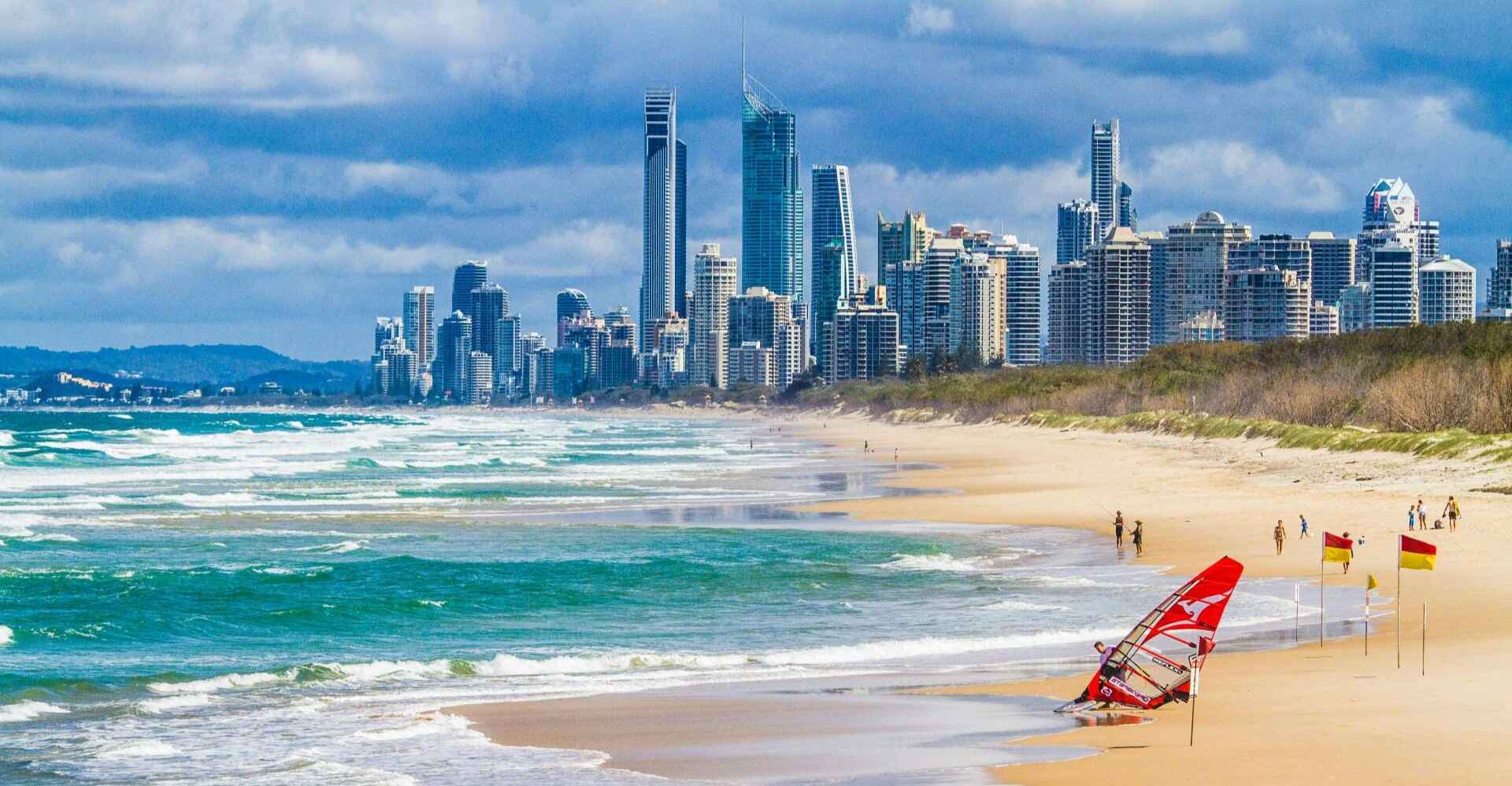 A beach in Australia with red and yellow beach safety flags on the shore and the city skyline in the background.
