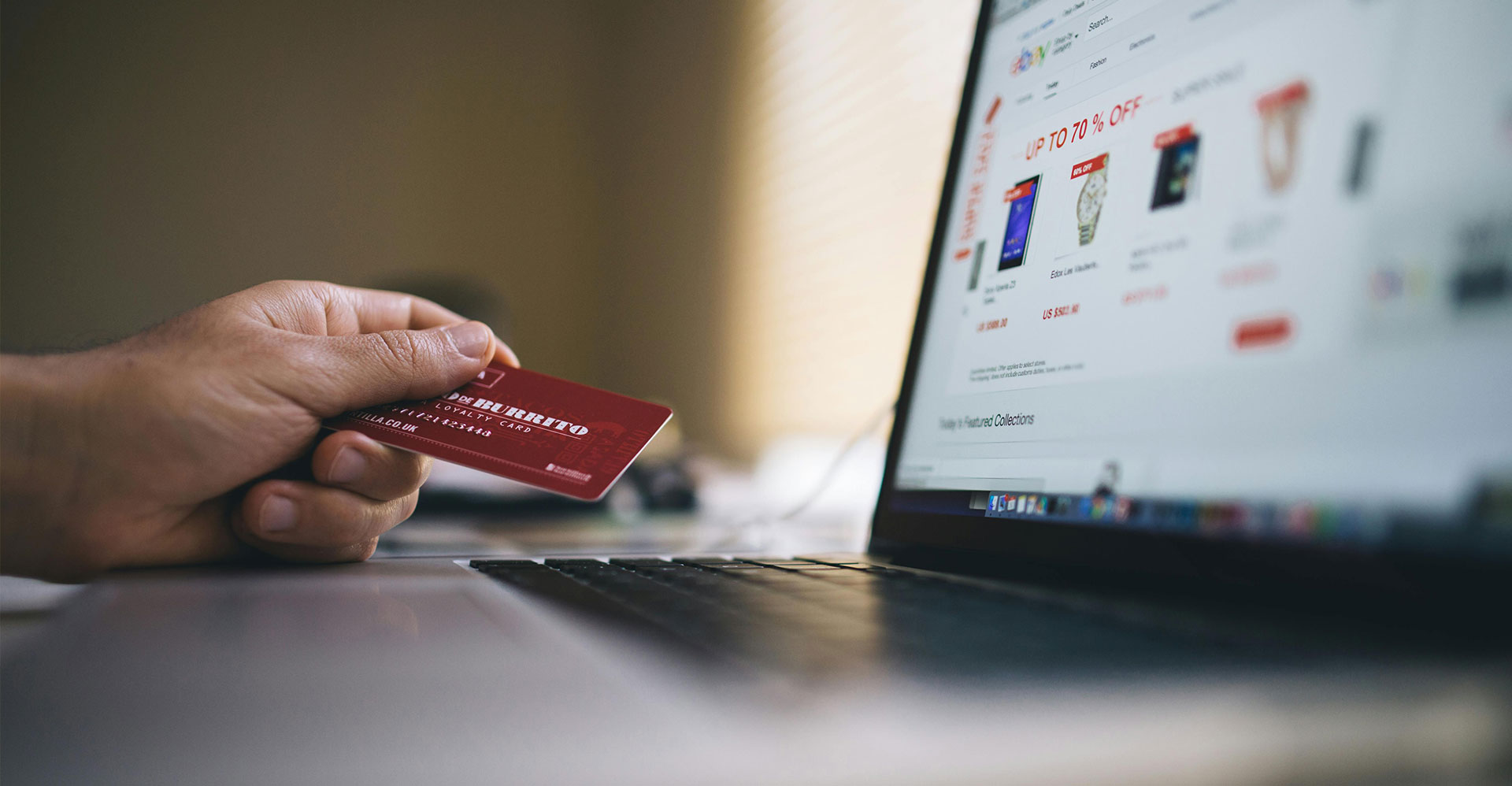 A consumer holds a credit card in front of a laptop while going through the e-commerce checkout process