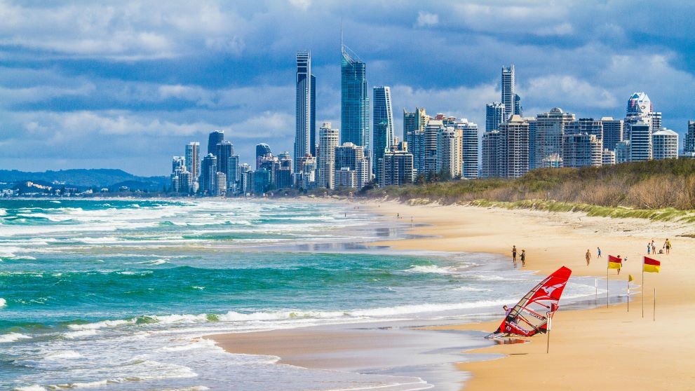 A beach in Australia with red and yellow beach safety flags on the shore and the city skyline in the background.