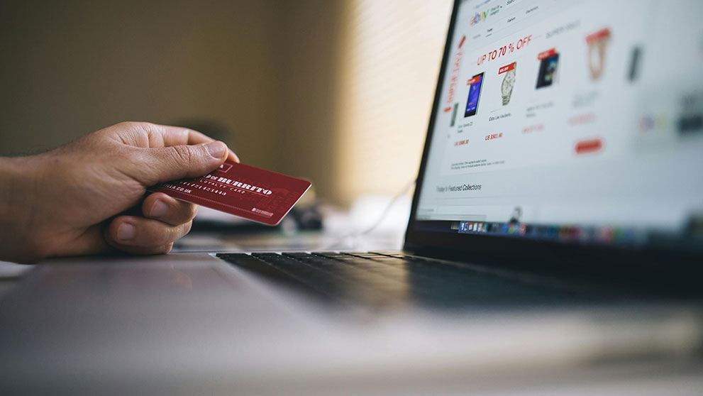 A consumer holds a credit card in front of a laptop while going through the e-commerce checkout process