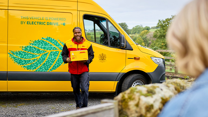  DHL 快递员在新能源货车前派送快件。