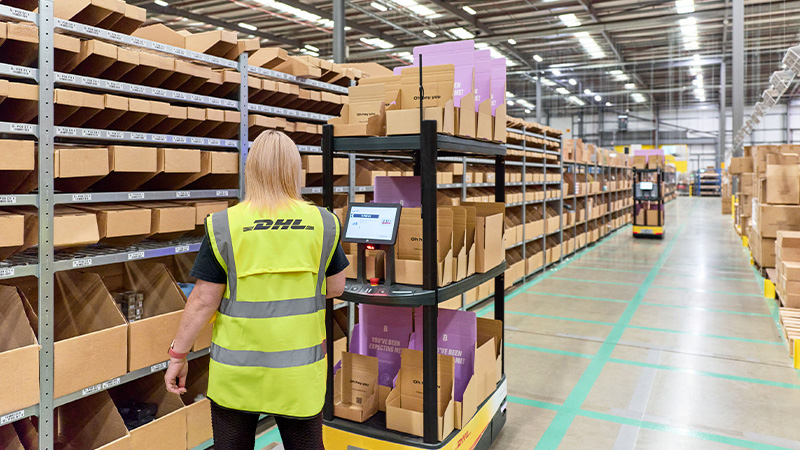 DHL 员工操控智能拣货车在仓储货架拣货。