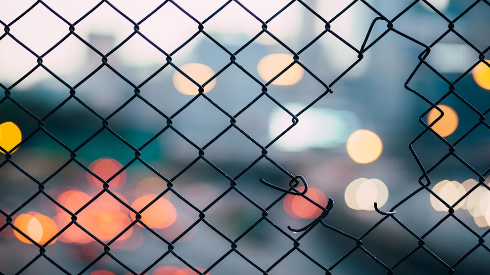 Hole in a metal fence with blurred lights