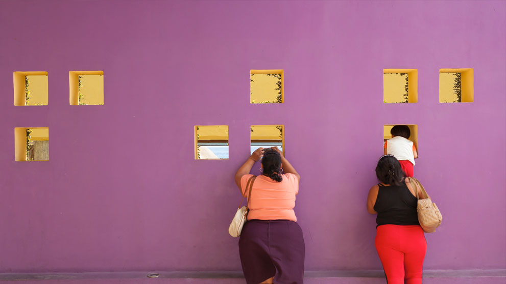 Purple wall with two women, one of which holding a child up to a window