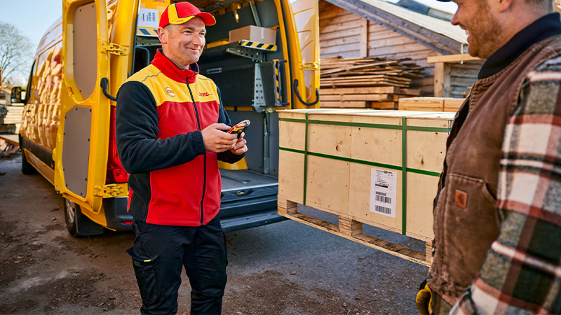 DHL courier scanning a wooden pallet whilst smiling at another man