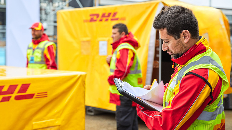 Three DHL workers standing on a car park with DHL branded pallets