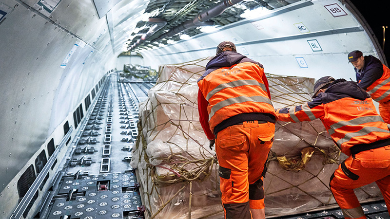 Three men pushing a large pallet onto an aeroplane