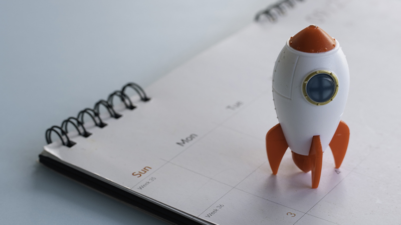 Toy rocket ship on a paper calendar symbolizing project deadlines and scheduled product launch dates.