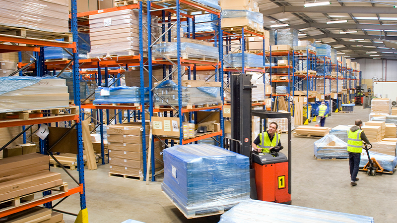 A wide shot of warehouse workers moving pallets with forklift.